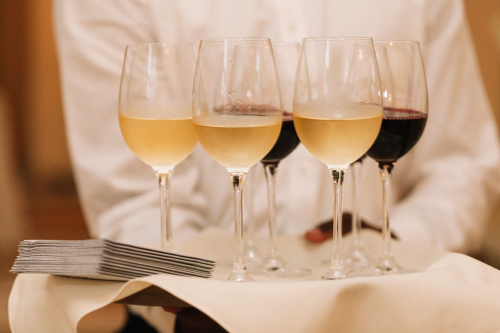 Konobar nosi poslužavnik sa čašama belog i crvenog vina u restoranu.