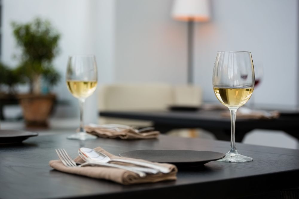 Dve čaše belog vina postavljene na elegantno serviranom stolu u restoranu.